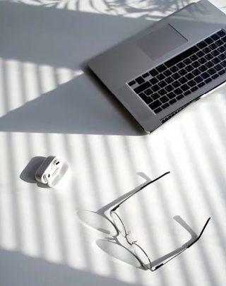 a laptop, airpods and glasses on a white surface